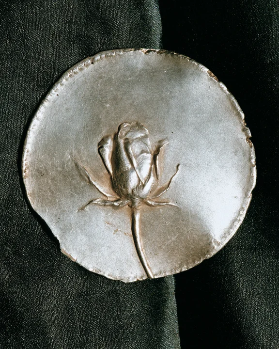 Ancient Greek silver coin from Rhodes showing a rose in relief, resting on dark linen