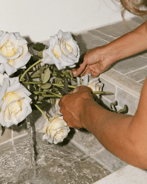 Hands trimming rose stems over a stone sink with water running