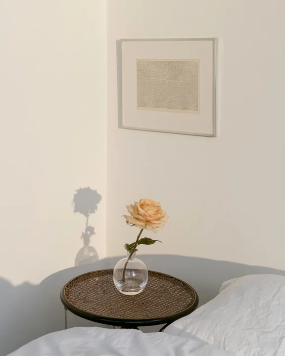 Bedroom corner in warm evening light with a single rose in a bud vase on a bedside table
