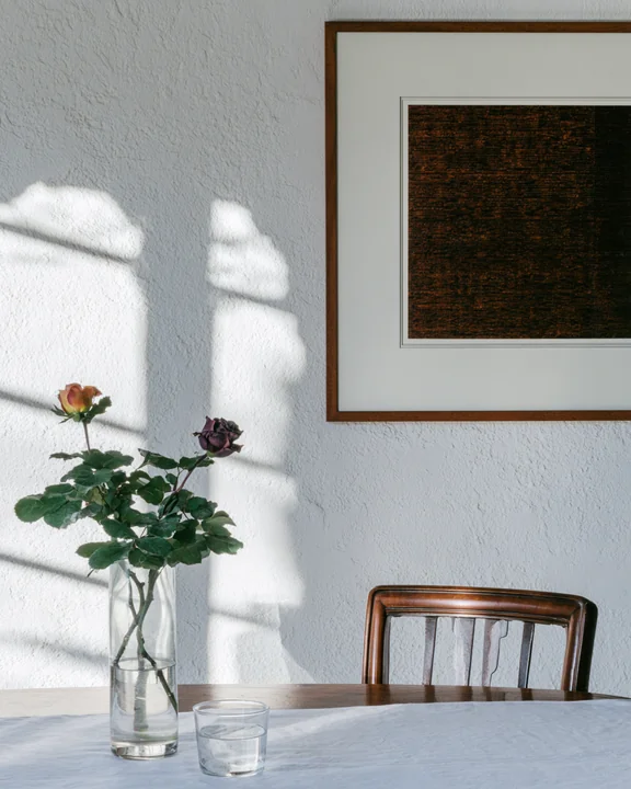 Textured plaster wall with a large framed artwork and a rose branch in a vase below it