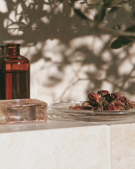 Bathroom shelf with a bar of rose soap, a small amber bottle and dried rosebuds in a dish