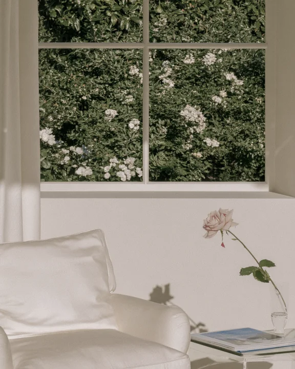 Reading corner with an armchair, a side table and one full-blown rose dropping a petal