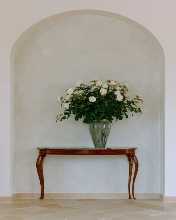 Entrance hall with a plaster wall, a narrow console and a tall vase of long-stemmed roses