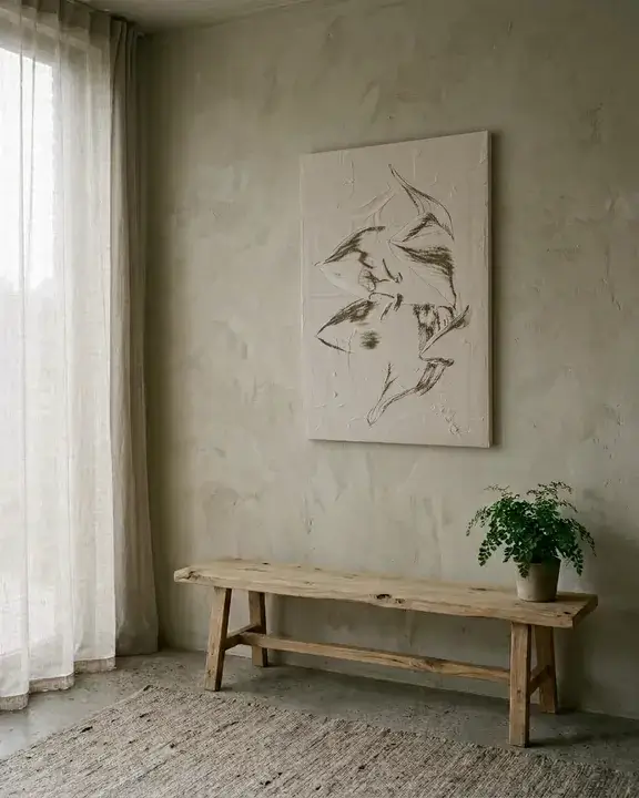 A pale textured relief hanging above a low raw oak bench, in soft diffused morning light with almost no shadow