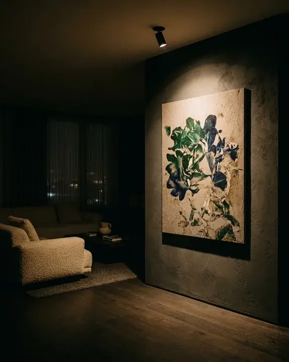A living room at night with every light off except one spot trained on a COBELIO relief, the rest of the room in warm darkness